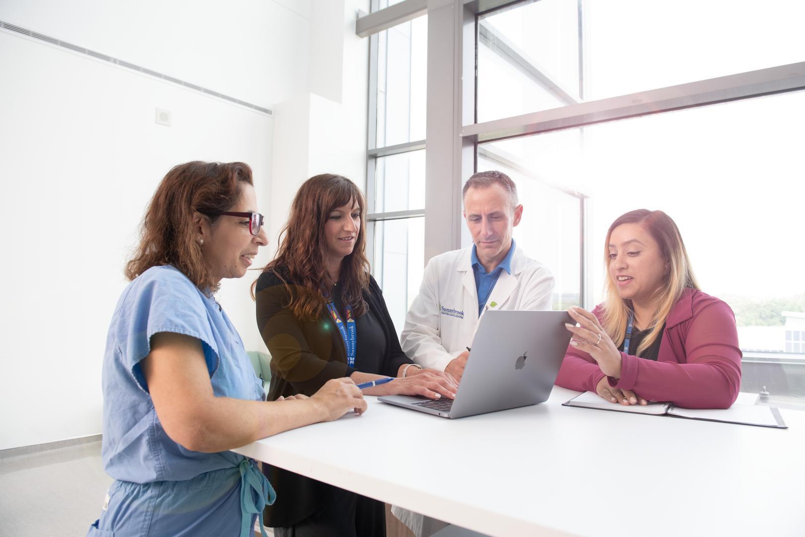 Four researchers huddled around a laptop in a well lit room