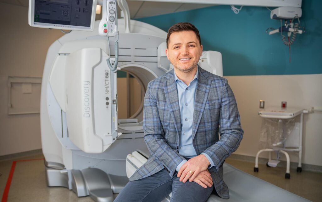 Dr. Alex Biliby sits in front of a CT Scanner.